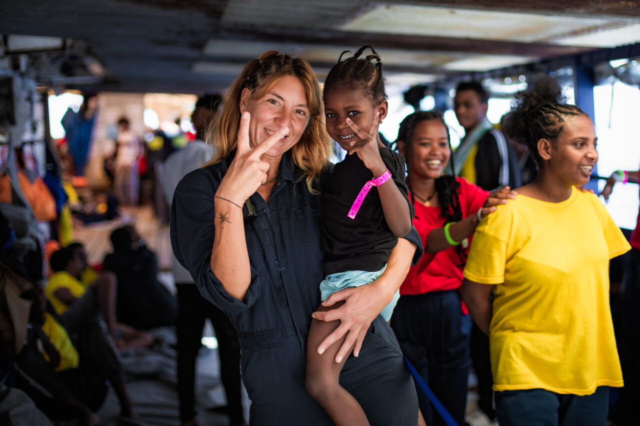 Das Foto zeigt ein Crew-Mitglied von SOS Humanity, das ein gerettetes Kind auf dem Arm trägt.