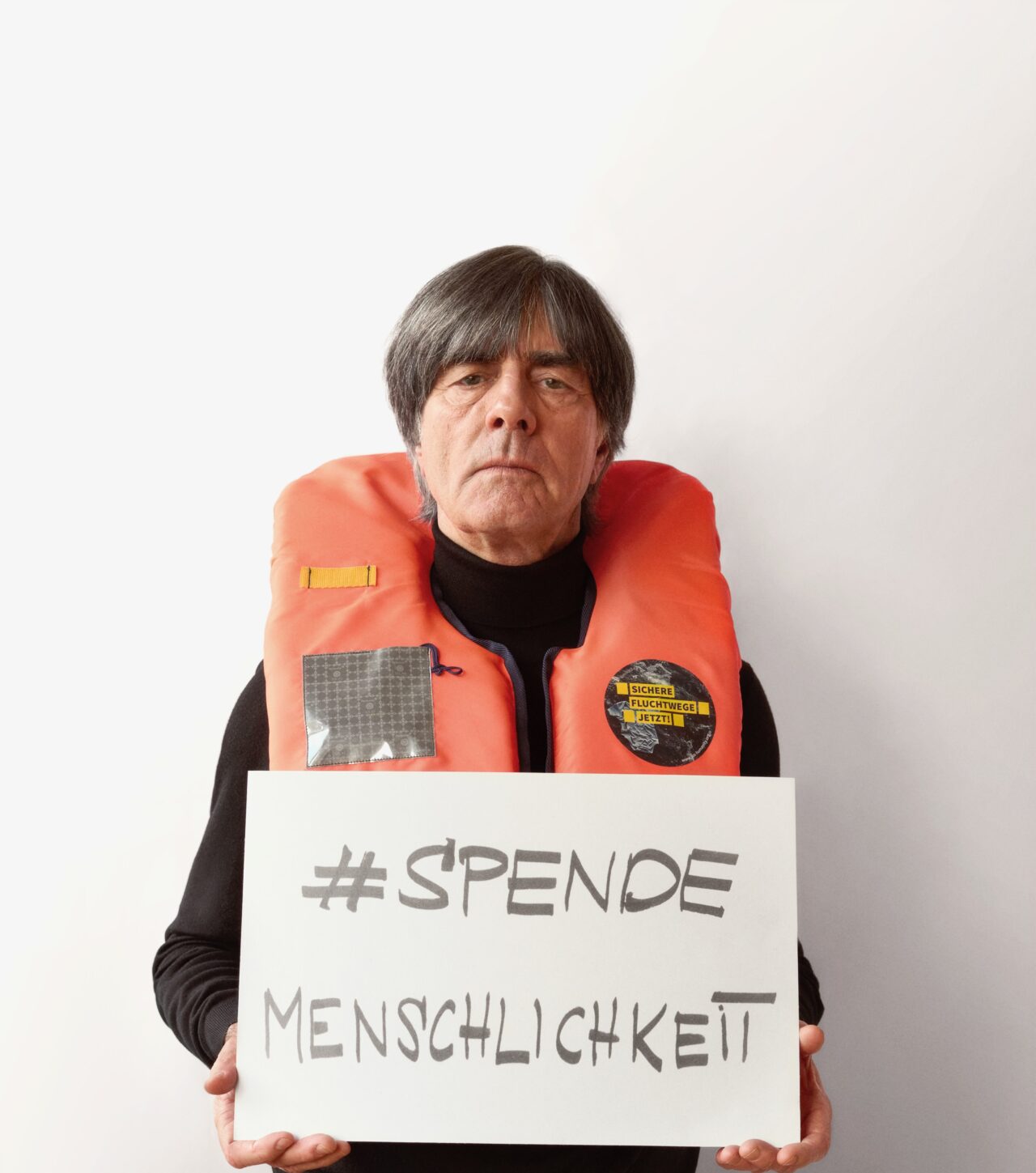 Jogi Löw mit Rettungsweste und dem Schild SPENDEMENSCHLICHKEIT