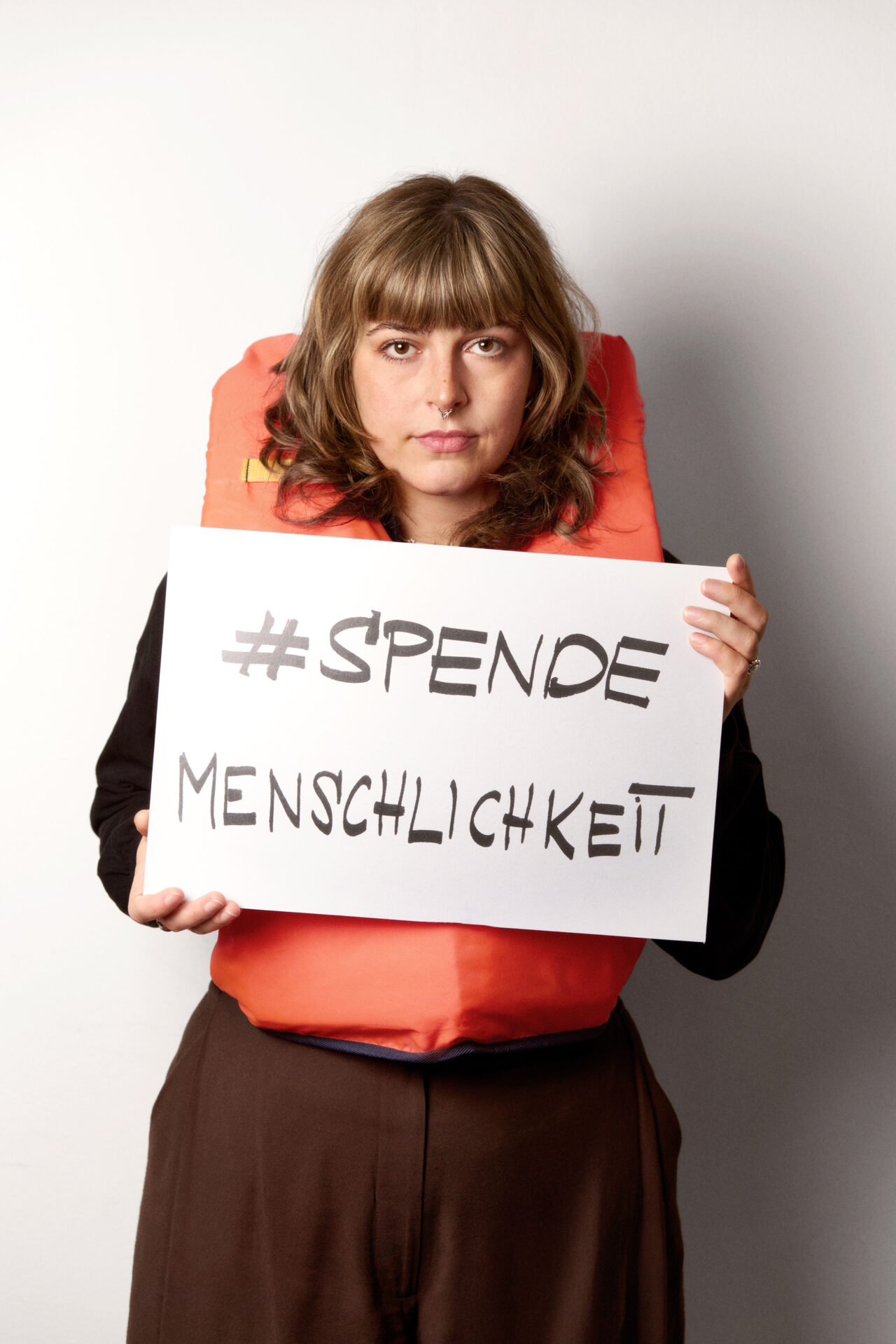 SOFFIE mit einer Rettungsweste und dem Schild 'SPENDEMENSCHLICHKEIT