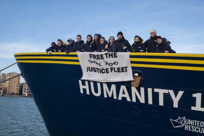 Crew an Bord des Rettungsschiffs Humanity 1 mit Plakat "Reffe the Justice Fleet"